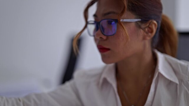 Businesswoman in glasses intently works at her office, reviewing documents and typing on her laptop. Her concentration highlights professionalism and efficient data analysis for corporate projects.