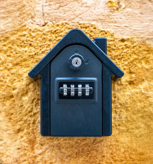 Close-up of a black key lockbox with a combination code mounted on a textured yellow wall. Used for...