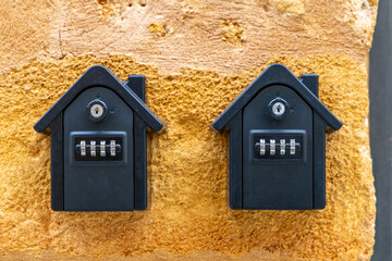 Two black key lockboxes with combination codes mounted on a textured yellow wall. Devices used for...