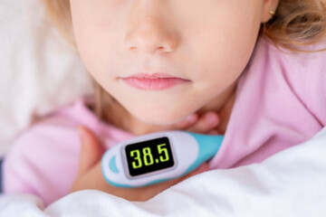 Close-up sick child lying in bed with digital thermometer, high temperature 38.5 C, childhood illness, Medical care and diagnosis, electronic device used to monitor high body temperature young patient