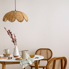 The stylish dining room with round table, rattan chair, lamp and kitchen accessories. Green leaf in...