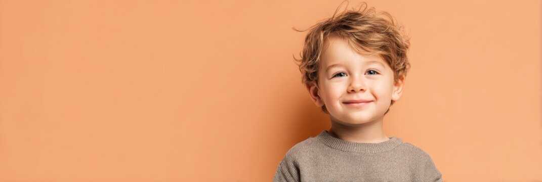 Cute young boy with curly hair smiles cheerfully against a warm orange background in a cozy indoor setting. Copy space