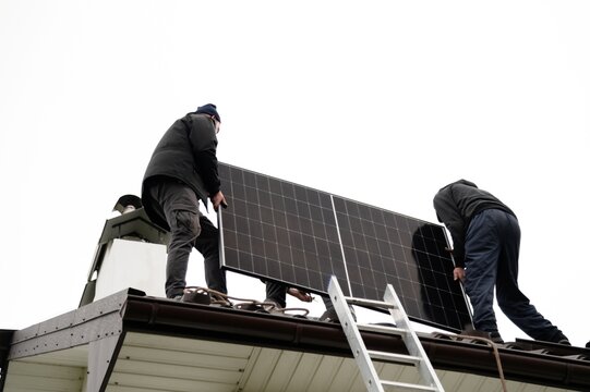 Workers installing solar panels on a rooftop during overcast weather in a residential area - Powered by Adobe