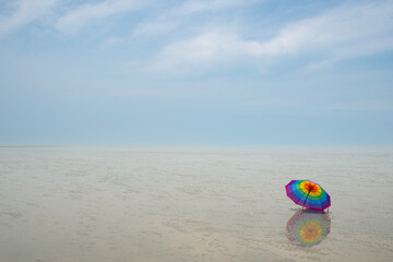 Obraz premium Solitary Rainbow Umbrella on Vast, Flat Mudflat Beach