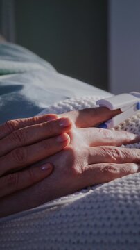 Wife strokes hand of elderly husband lying on hospital bed