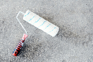 A paint roller with a white and blue pattern rests on a textured concrete surface, ideal for home improvement or renovation projects.