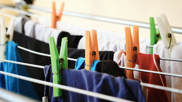 Close-up of colorful clothes hanging on drying rack with bright plastic clothespins. Domestic chores, household routine