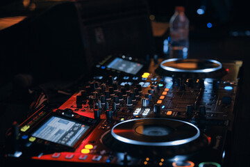 Professional DJ mixer setup with illuminated controls, dual turntables and glowing buttons in dark nightclub environment. Nightlife, music, creativity