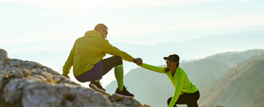 Two climbers assist each other while scaling a rocky mountain at sunrise. The golden light highlights their effort and teamwork on the challenging path