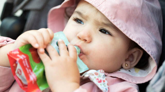 Toddler eating fruit puree from a pouch outdoors