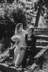 Bride and groom sitting on stone steps, surrounded by lush greenery, sharing a joyful moment, capturing the essence of love and celebration in a beautiful outdoor setting