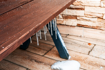 Icicles hanging from a wooden table on a stone patio. Snow is present on the ground, creating a winter scene