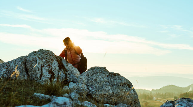 Hiker climbs rocky terrain at sunset in mountainous landscape under clear sky - Powered by Adobe