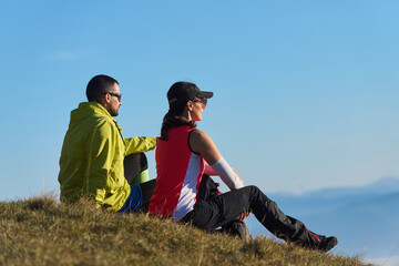 Two hikers enjoy a peaceful moment on a hillside overlooking a stunning landscape during a sunny day
