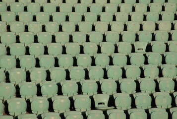 Rows of empty turquoise stadium seats illuminated by golden-hour light. A clean, repetitive pattern ideal for sports, events, architecture, recreation, or venue-related visual concepts.
