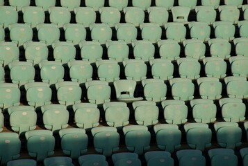 Rows of empty turquoise stadium seats illuminated by golden-hour light. A clean, repetitive pattern ideal for sports, events, architecture, recreation, or venue-related visual concepts.