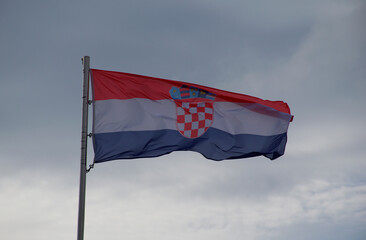 Vibrant Croatian flag with coat of arms waving in strong wind beneath a dramatic cloudy sky. Perfect for themes of patriotism, national identity, Europe, travel, and political or cultural symbolism.