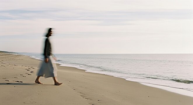 Artistic long exposure of a solitary person walking barefoot on a vast, sandy beach, the motion blur creating a dreamy, contemplative mood against the calm ocean and sky