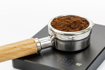 Close-up of metal portafilter filled with espresso coffee grounds on digital scale displaying weight measurement