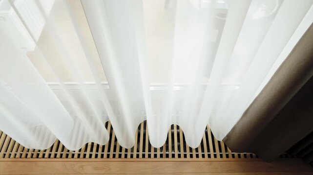 In-floor convector heating system with elegant wooden grille and flowing sheer curtains, showcasing modern trench HVAC integration in a bright minimalist interior