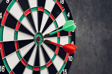 Darts on Dartboard with One Red and One Green Dart in Center