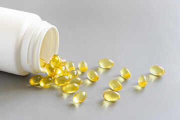 Yellow softgels (gelatin capsules) and bottle on a grey close up. Omega 3 Fish oil or garlic oil