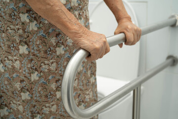 Asian elderly woman patient use toilet support rail in bathroom.
