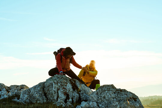 Two hikers climbing a rocky peak under a clear blue sky during early morning hours in the mountains