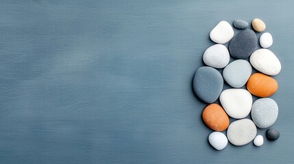 A collection of smooth, rounded stones in various colors and sizes are artfully arranged on a textured, muted blue surface.