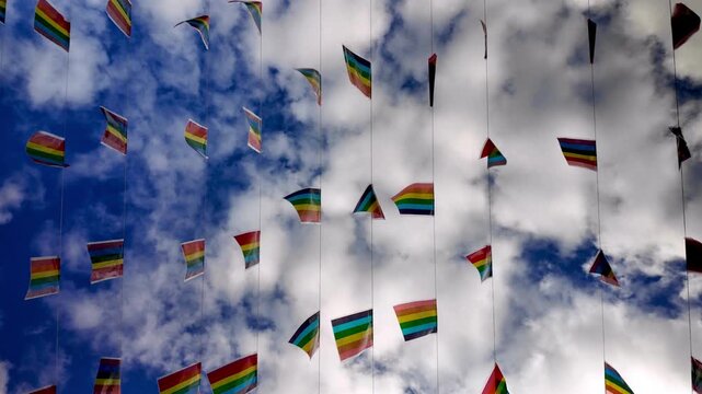 Colorful LGBT pride flag garland hanging on strings and fluttering in the wind against a beautiful blue sky with fluffy white clouds, celebrating love, freedom, and human rights