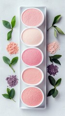 A collection of cosmetic powders in shades of pink and purple, arranged in small white bowls with decorative green leaves.