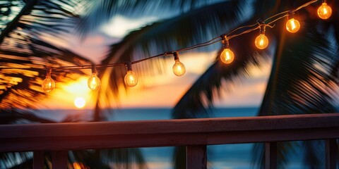 String of light bulbs hanging from a palm tree, casting a warm glow over a tropical beach scene with the ocean in the background.