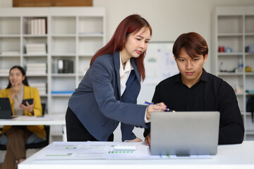 Asian businesswoman pointing at laptop helping intern in office.
