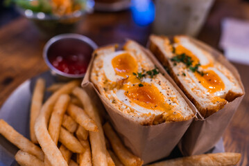 Close view of a halved Japanese egg sandwich with jammy yolks, herbs, thick fries, and ketchup in Tokyo, warm tones and shallow depth of field emphasize texture.