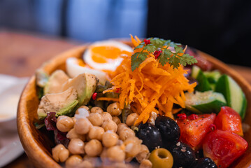 Close up of a Tokyo cafe salad bowl with chickpeas, cherry tomatoes, cucumber, black and green olives, avocado, shredded carrot, herbs, and a soft boiled egg.
