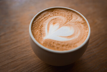 A close up cup of latte with heart latte art rests on a wooden table in a Tokyo coffee shop, warm tones and smooth foam suggest a cozy pause during city travel.