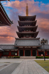 A five tier pagoda rises over Senso ji Temple in Asakusa, Tokyo, with red halls, tiled roofs, and a lantern streetlight in a near empty courtyard at dusk.
