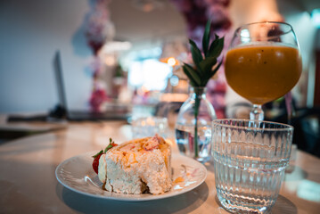 A Tokyo cafe table shows strawberry shortcake on a white plate, a ribbed glass of water, a mango juice goblet, and a tiny vase, with soft focus modern decor in view.