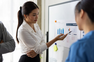 Businesswoman using pen pointing at graph and chart on whiteboard during a presentation to colleagues in the office.
