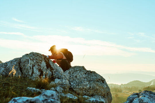 Hiker climbs rocky terrain at sunset in mountainous landscape under clear sky