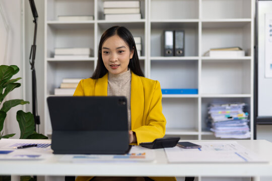 Young professional woman sitting at office desk and using digital tablet, working with financial charts and graphs, online business meeting, modern workplace.