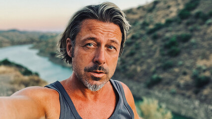 Middle aged tanned man with half long blond hair and grey stubble beard in singlet shirt walking outdoors during golden hour. Hills of Almogia, Malaga, Andalusia, Spain.