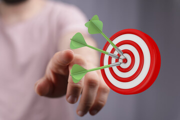 Hand pointing towards a dartboard with three darts in the center, symbolizing achievement and...