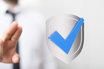 A businessperson's hand reaching towards a shield with a check mark, representing protection, validation, and security.