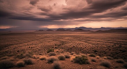 A dramatic storm gathers over a vast desert landscape at sunset, with rain falling on distant mountains under a moody, cloud-filled sky