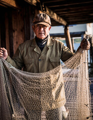 Fototapeta premium Old fisherman holding net under warm morning light