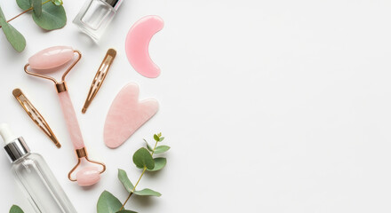 Rose quartz facial massage tools and glass skincare bottles arranged with eucalyptus leaves on a bright minimal white background