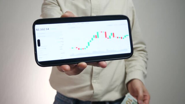 Hands of a successful professional connecting digital success with tangible cash. The phone screen shows clear financial growth, while the other hand celebrates with a gesture of victory using the