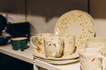 Colorful printed cups on handmade tableware store shelf with space for text.