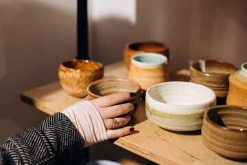 Woman touching handmade tableware while choosing items in craft store.